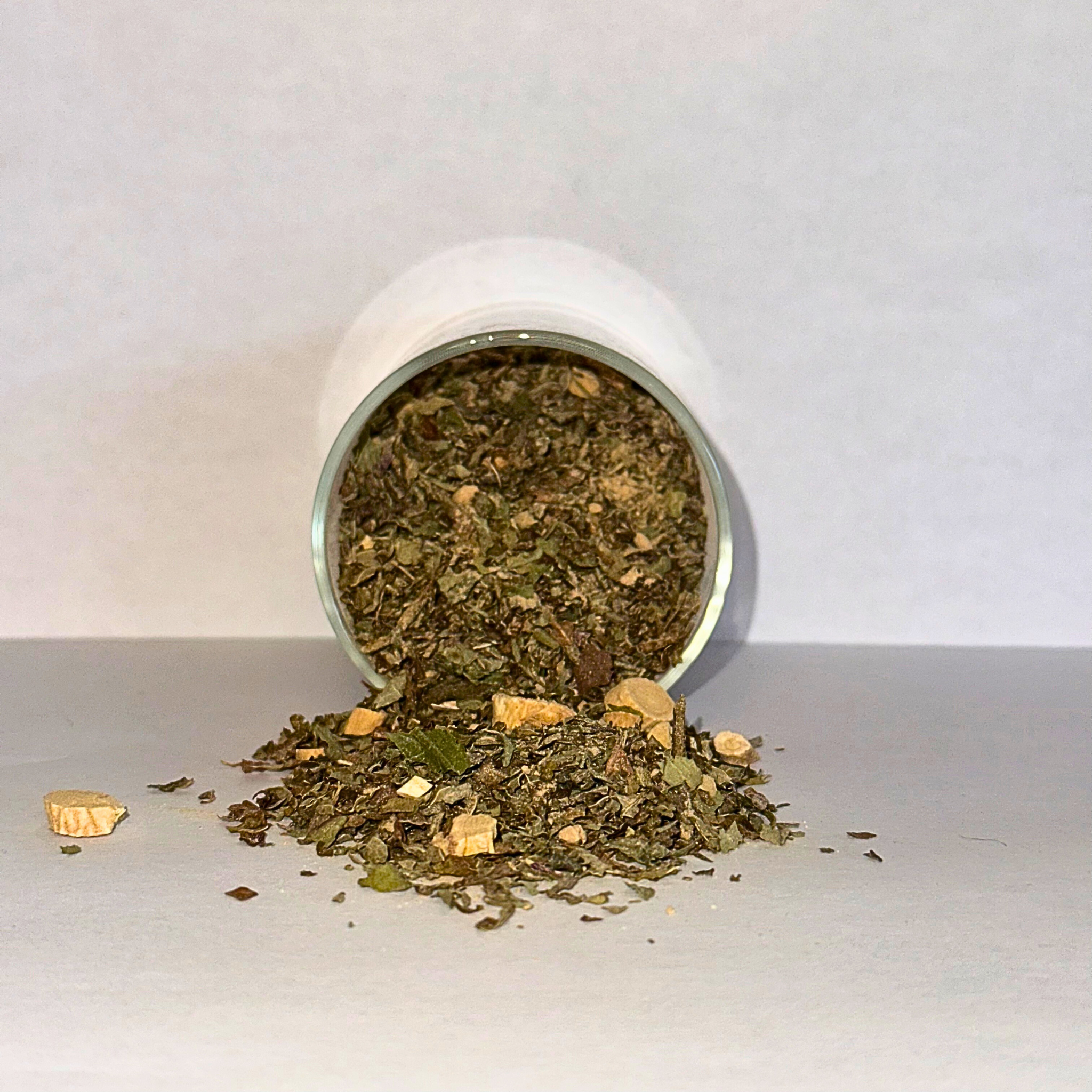 Spilled container of dried herbs on a white surface with a white background