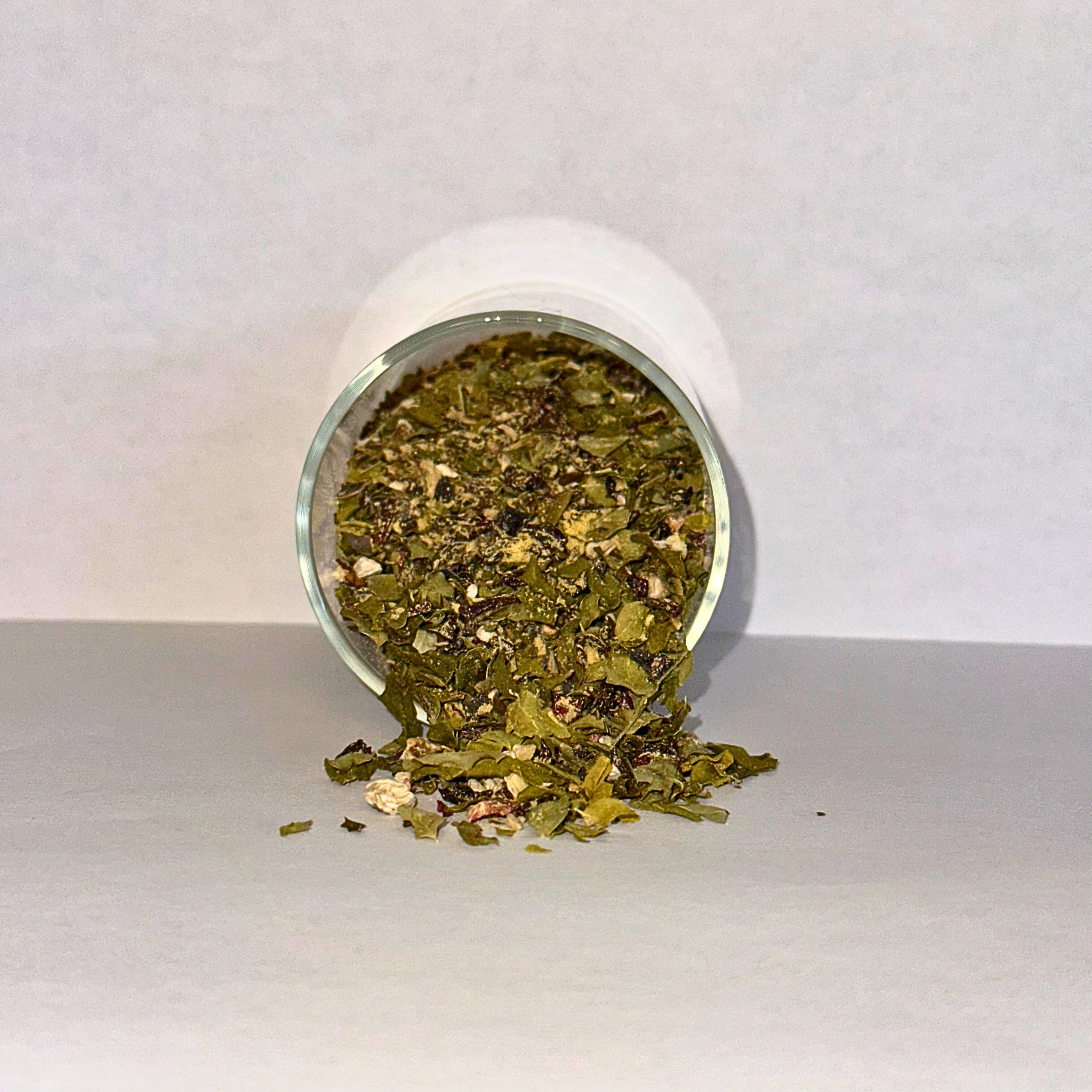 Loose leaf green herbal tea leaves with roots and powder spilling out of a glass jar