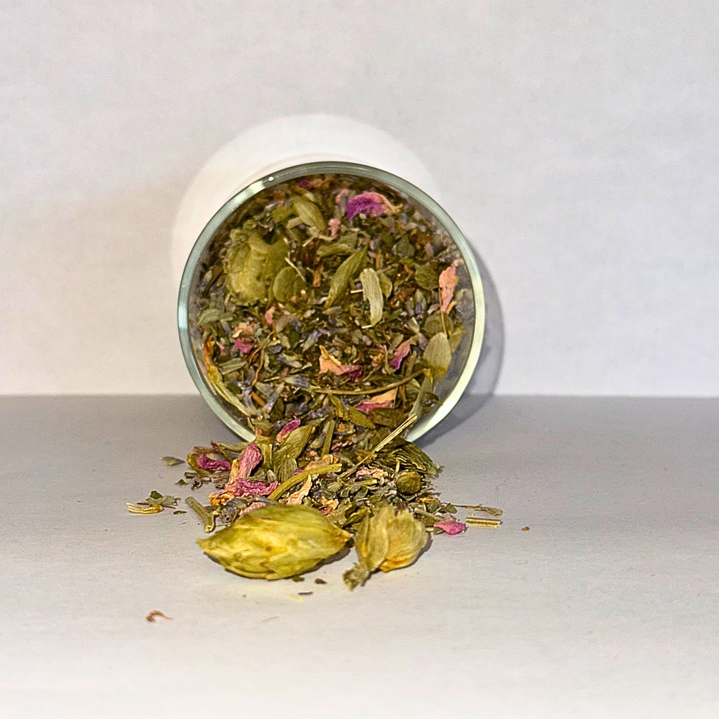 Tea leaves with pink petals spilling out of a white container on a light gray background